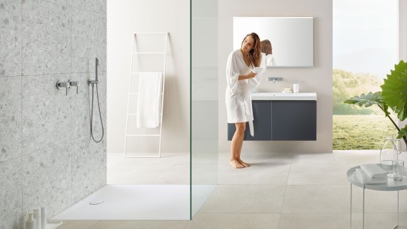 Femme se séchant les cheveux avec une serviette dans une salle de bains avec douche ouverte et grands carreaux de style terrazzo