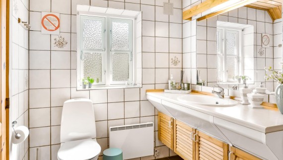 L’ancienne salle de bains avec WC au sol, carrelage blanc et meubles en bois (© @triner2 et @strandparken3)